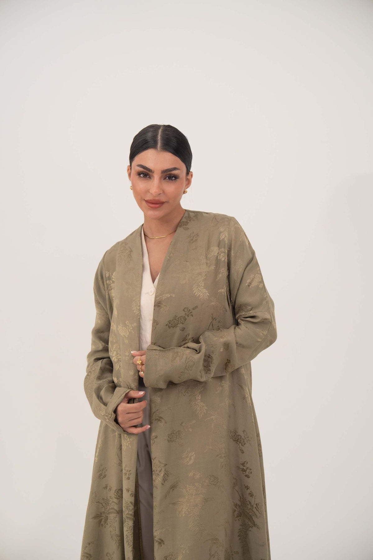 Woman wearing soft olive green silk Liora abaya with collarless, open-front design and ruched full-length sleeves.