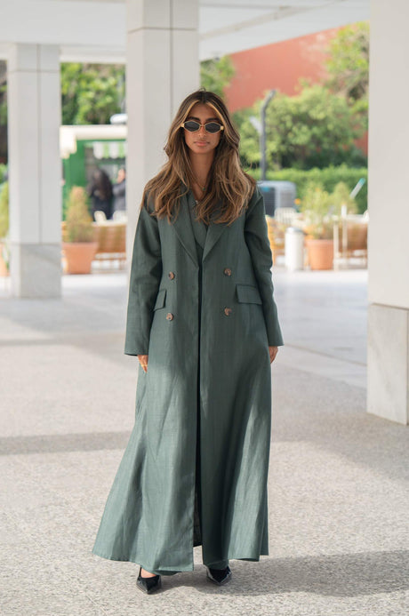 Woman wearing a dark green linen blazer abaya with brown trim and double buttons walking outdoors