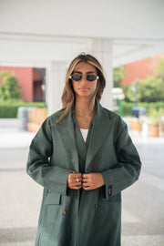 Woman wearing a dark green linen blazer with structured cut and brown trim on collar and edges