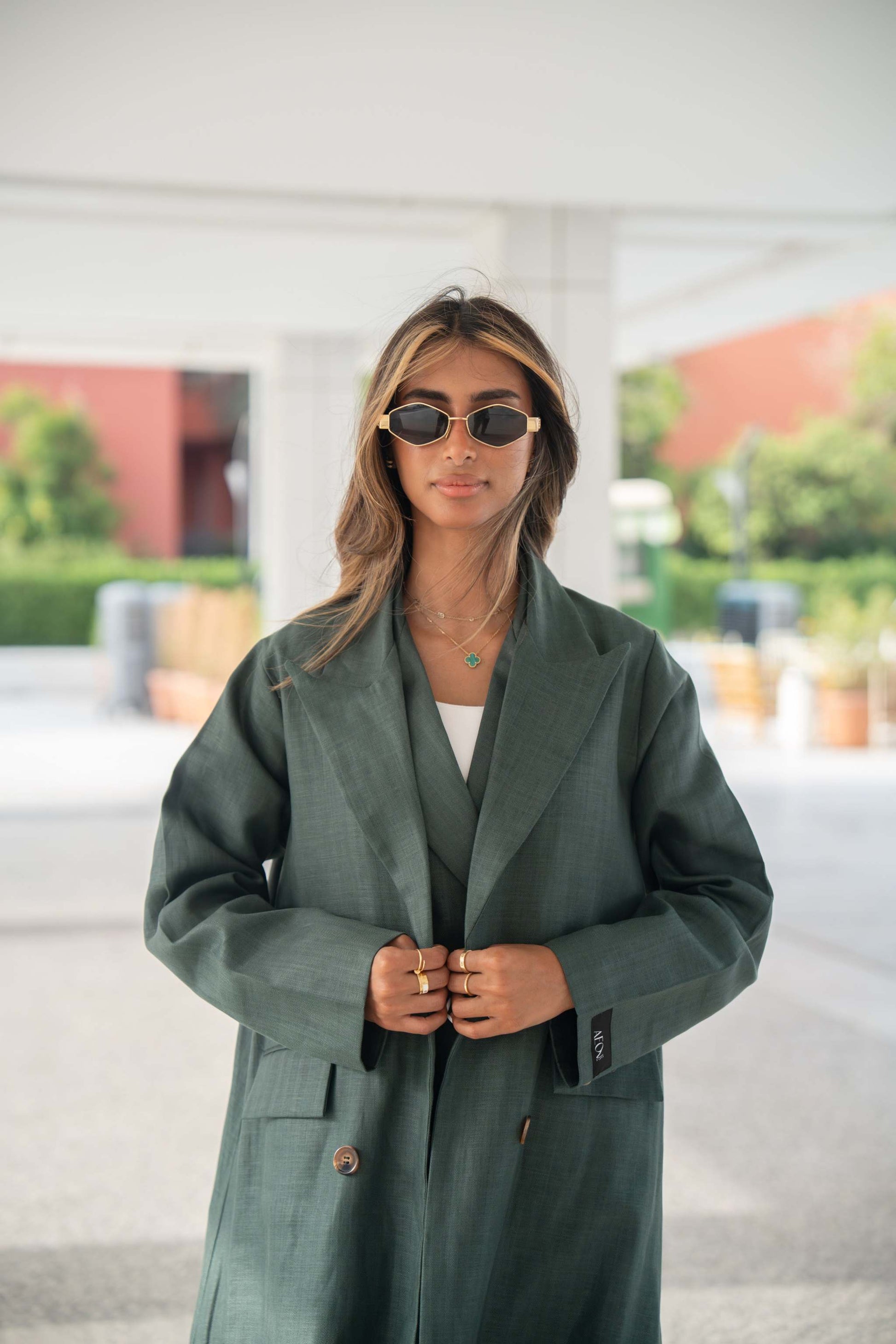 Woman wearing a dark green linen blazer with structured cut and brown trim on collar and edges