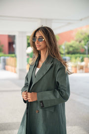 Woman wearing a dark green linen blazer with brown trim and structured cut outdoors