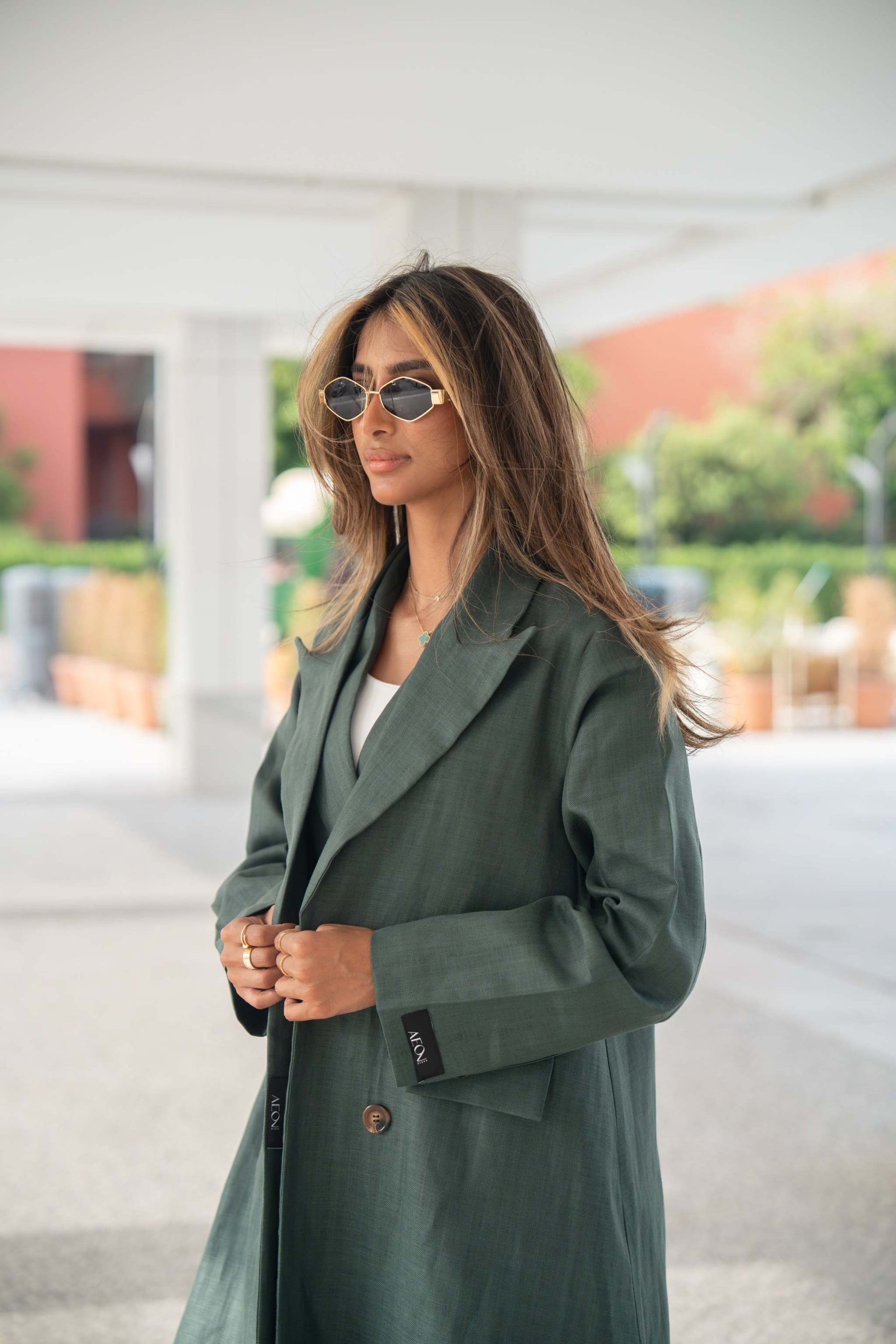 Woman wearing a dark green linen blazer with brown trim and structured cut outdoors