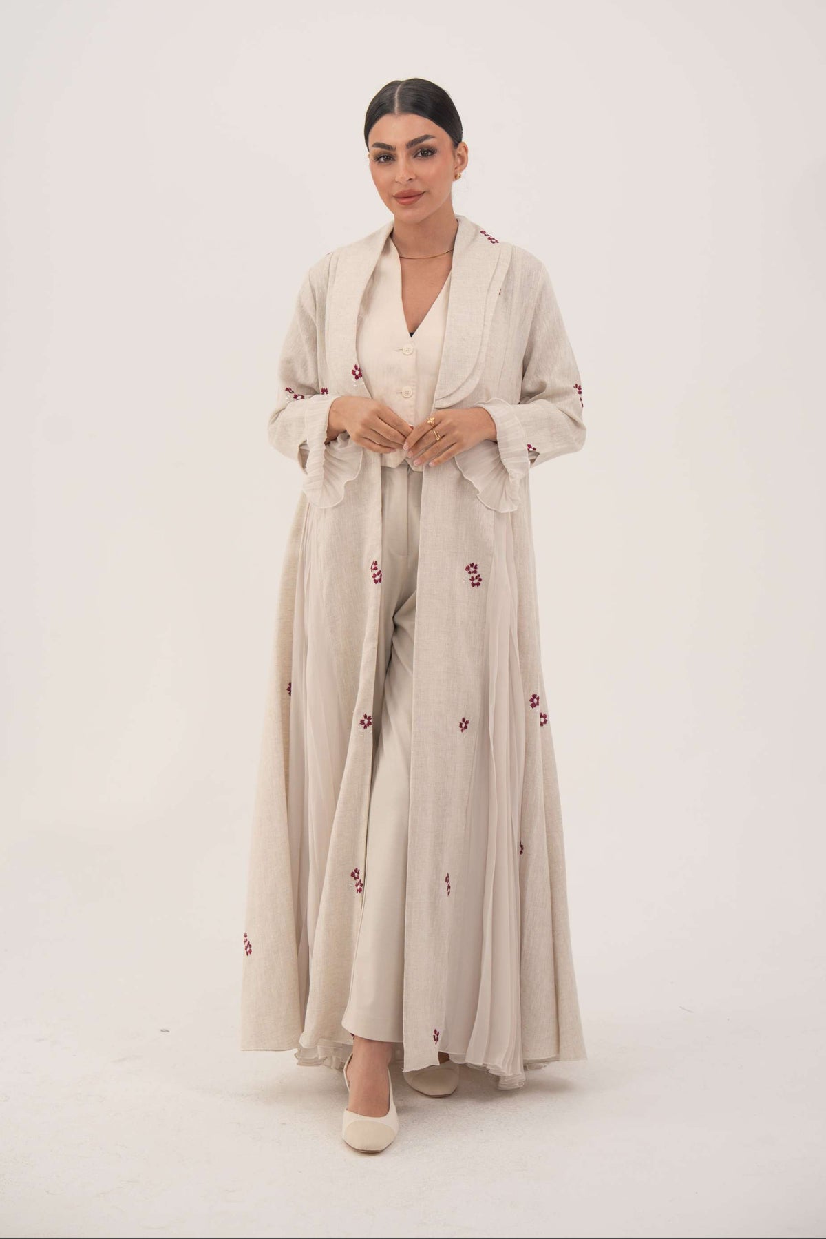 Woman wearing elegant natural beige linen abaya with burgundy floral embroidery and chiffon pleats.