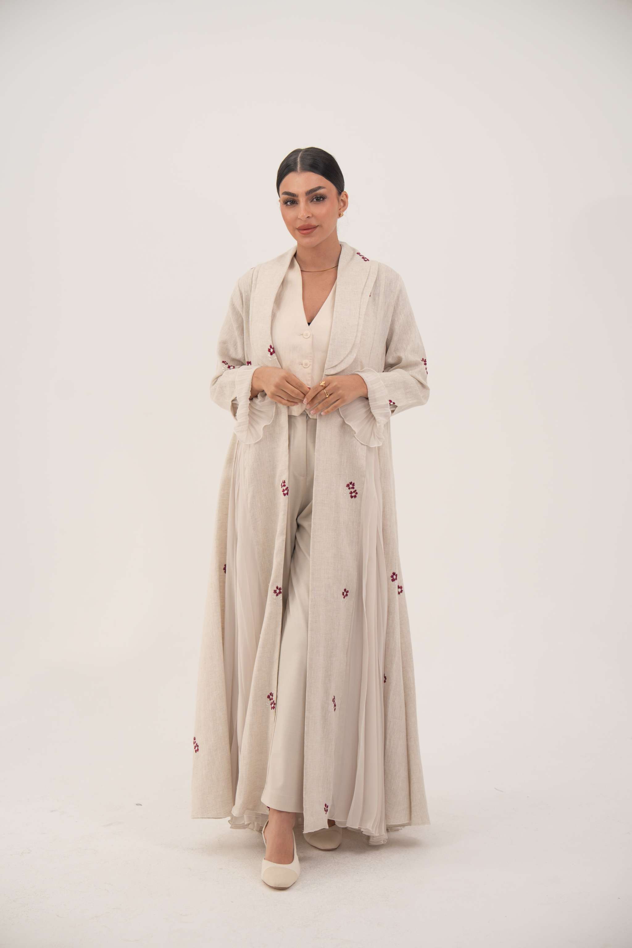 Woman wearing elegant natural beige linen abaya with burgundy floral embroidery and chiffon pleats.