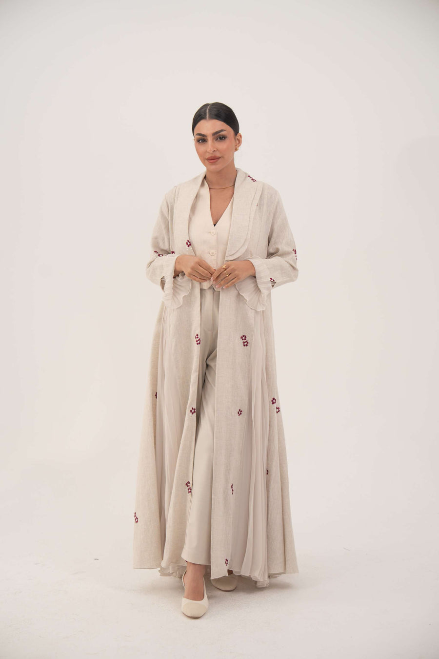 Woman wearing elegant natural beige linen abaya with burgundy floral embroidery and chiffon pleats.