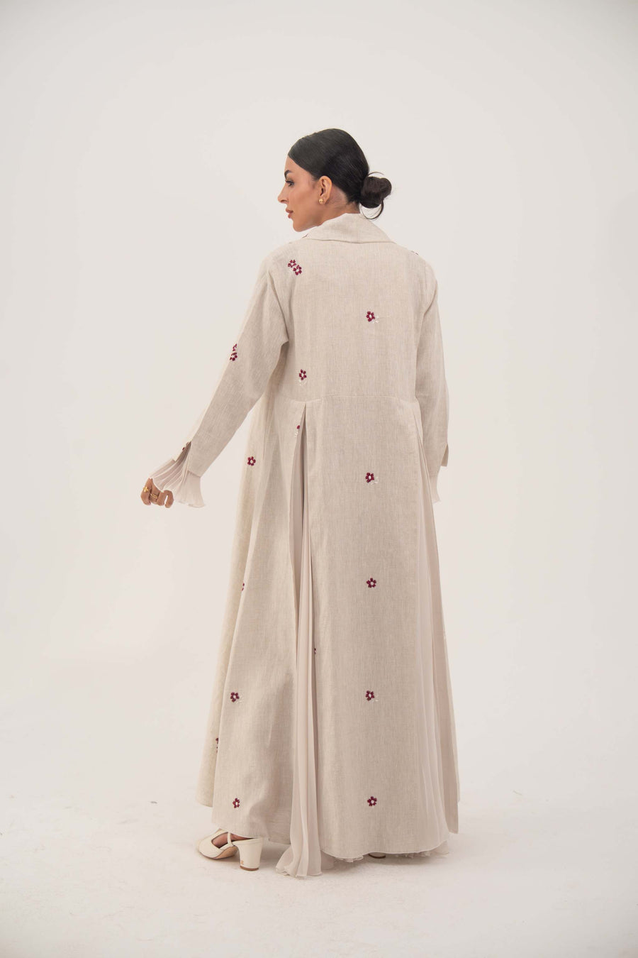 Beige linen abaya with burgundy floral embroidery and soft chiffon pleats, featuring a shawl collar and flowing design.