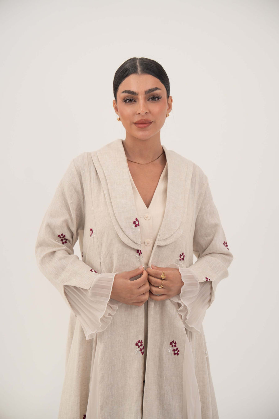 Natural beige linen abaya with burgundy floral embroidery, chiffon pleats, and shawl collar for an elegant feminine look.