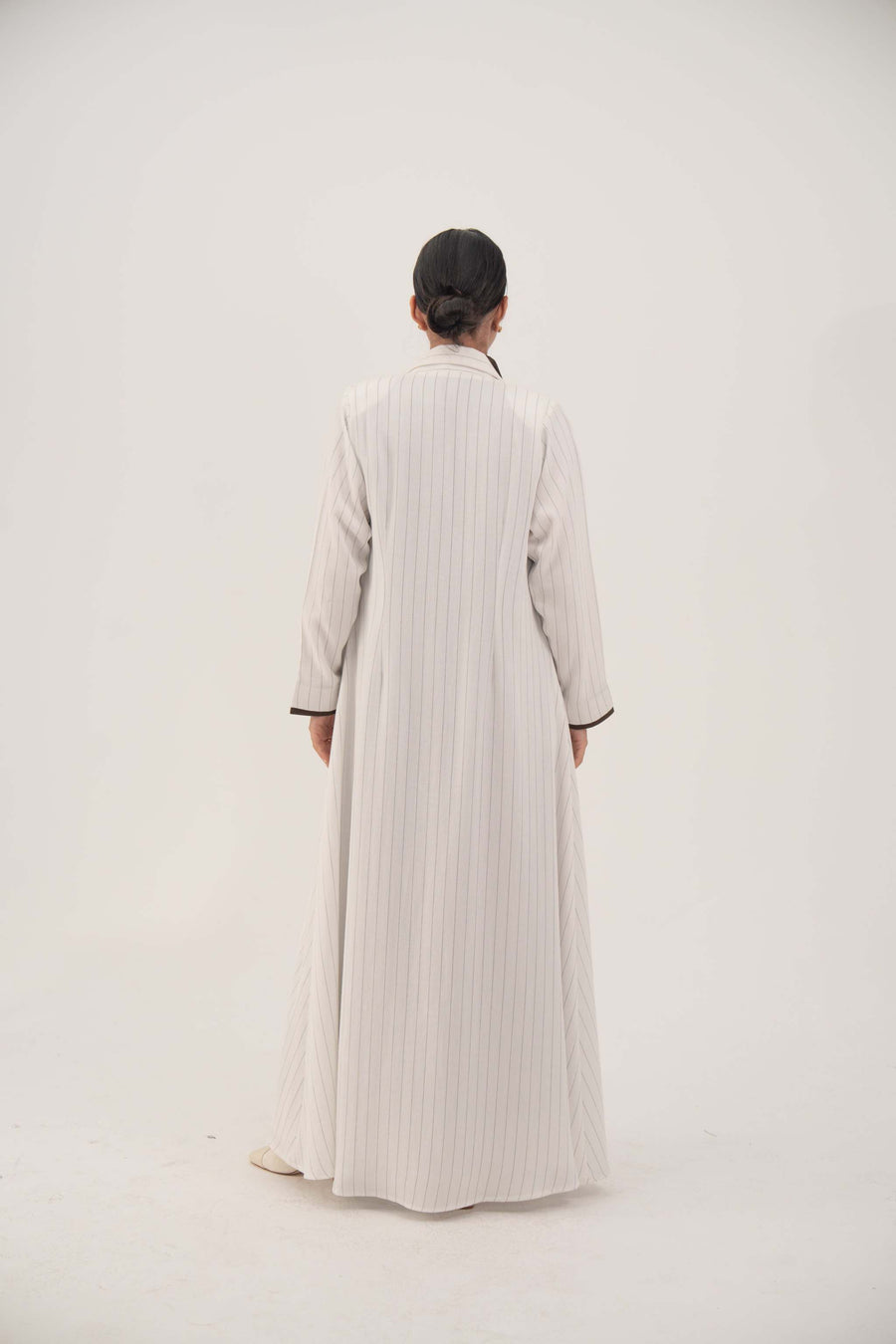 Back view of elegant white linen abaya with light grey pinstripes, dark brown inner cuffs, sharp lapel, and slightly flared long hem - Elegant abaya
