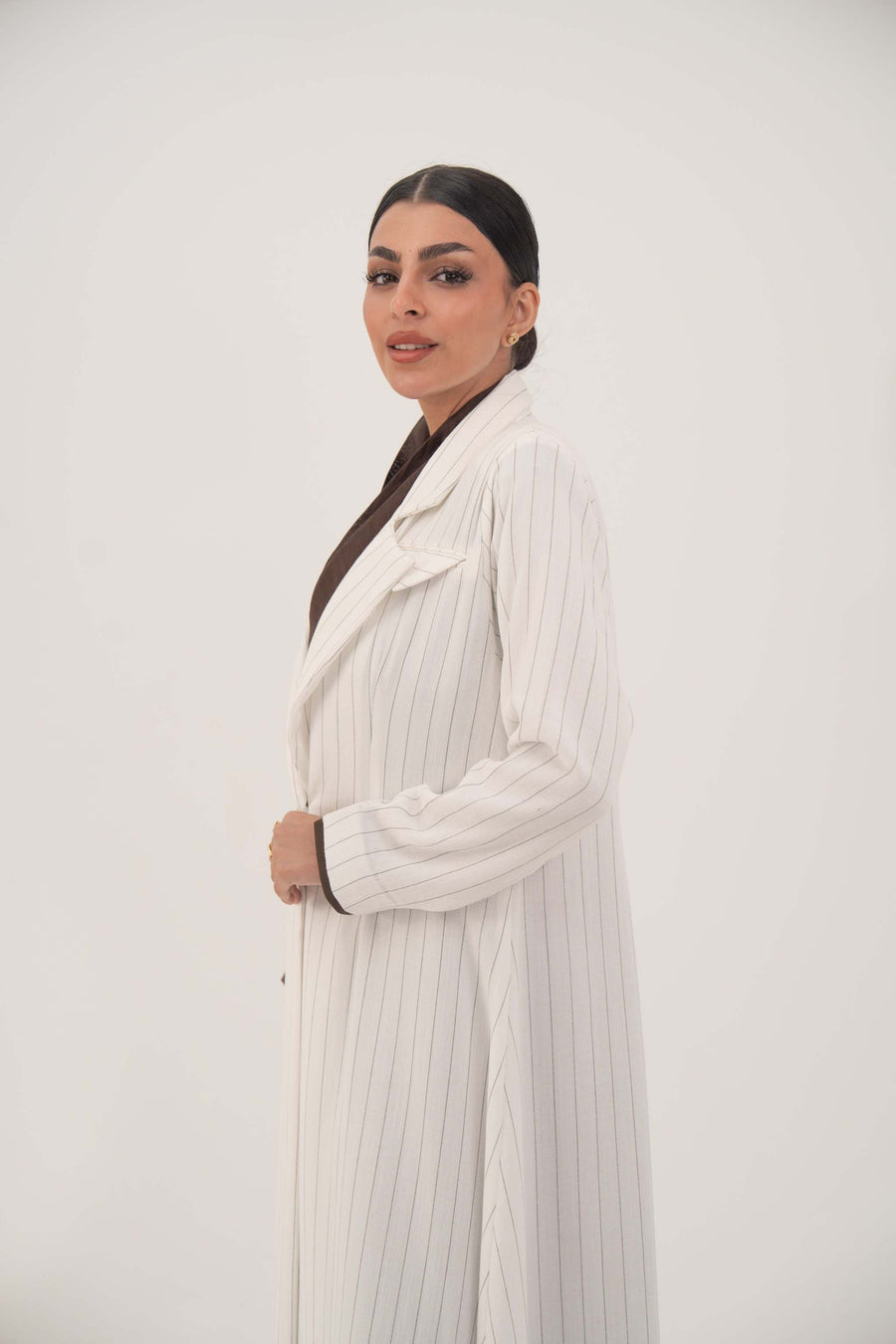 Elegant abaya in white linen with grey pinstripes, blazer-inspired cut, single-button closure, and dark brown inner cuffs, worn by a woman.