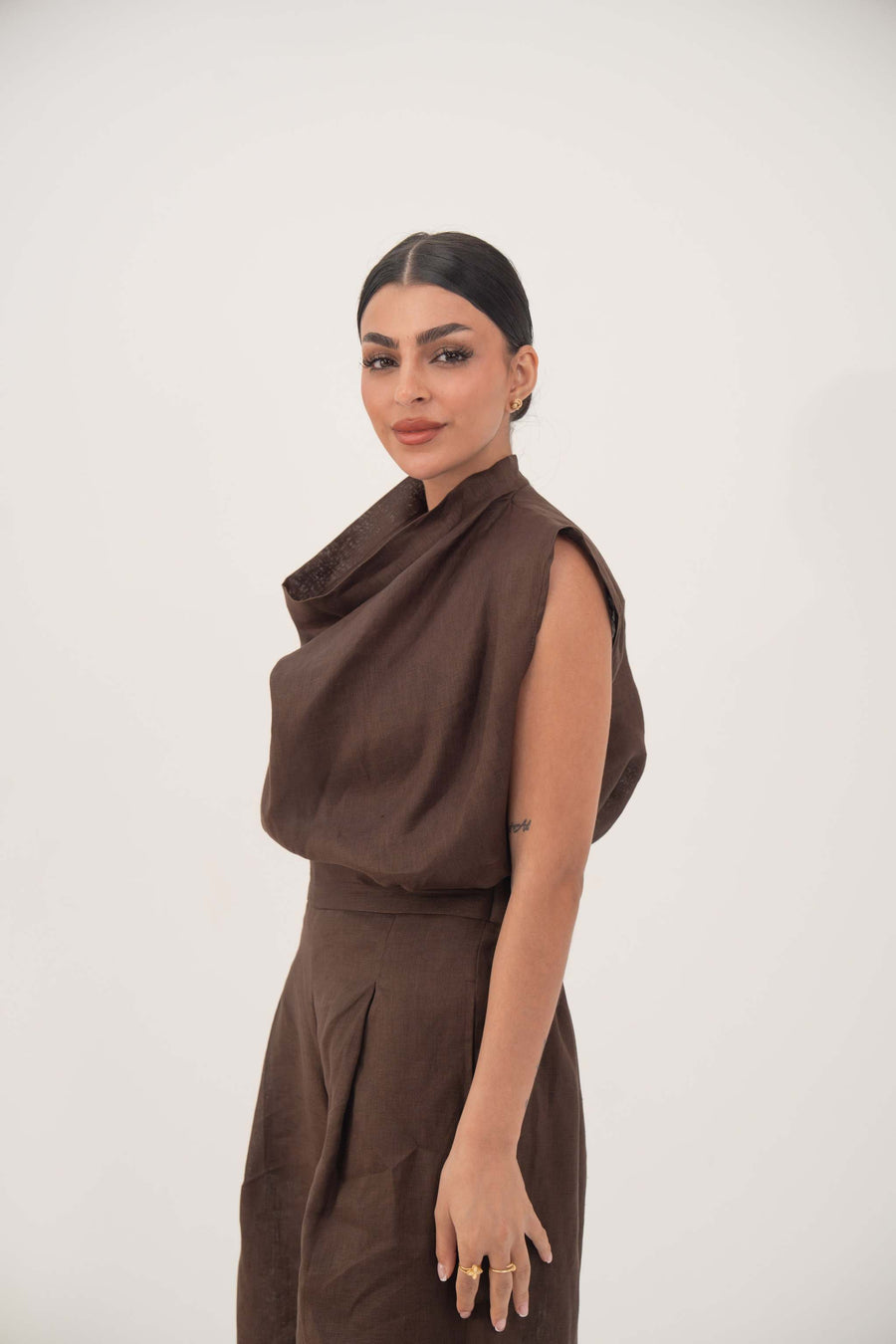 Woman wearing sleeveless brown linen blouse with cowl neckline and structured shoulders