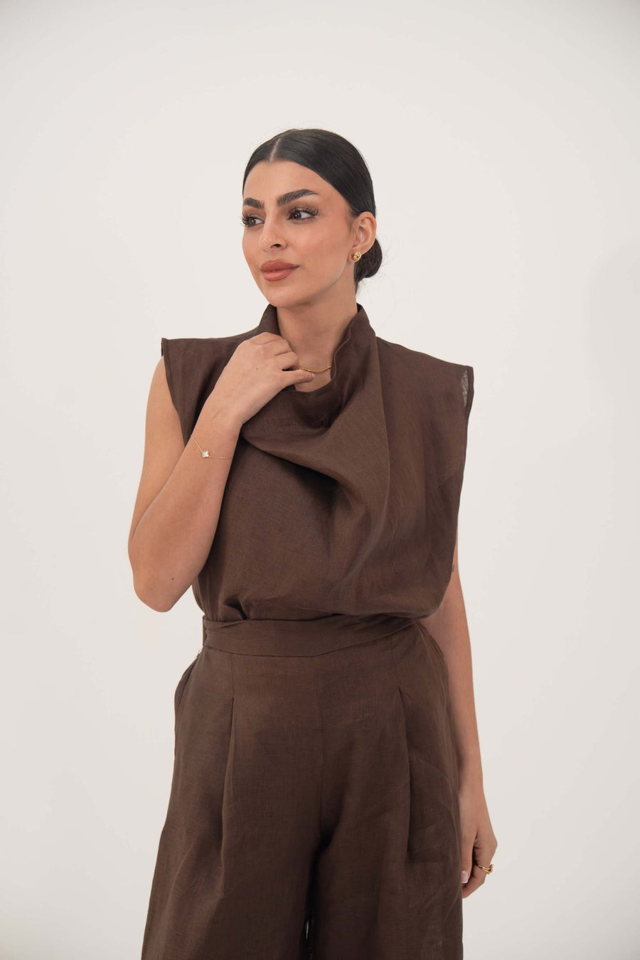Woman wearing a sleeveless brown linen blouse with a soft cowl neckline and structured shoulders