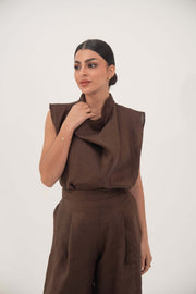 Woman wearing sleeveless brown linen pleated blouse with draped neckline and matching pants