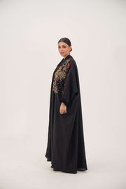 Woman wearing premium black linen abaya with multicolored red, gold, and navy shak embroidery and red trim, loose flowing bisht silhouette - abaya crafted from premium black linen