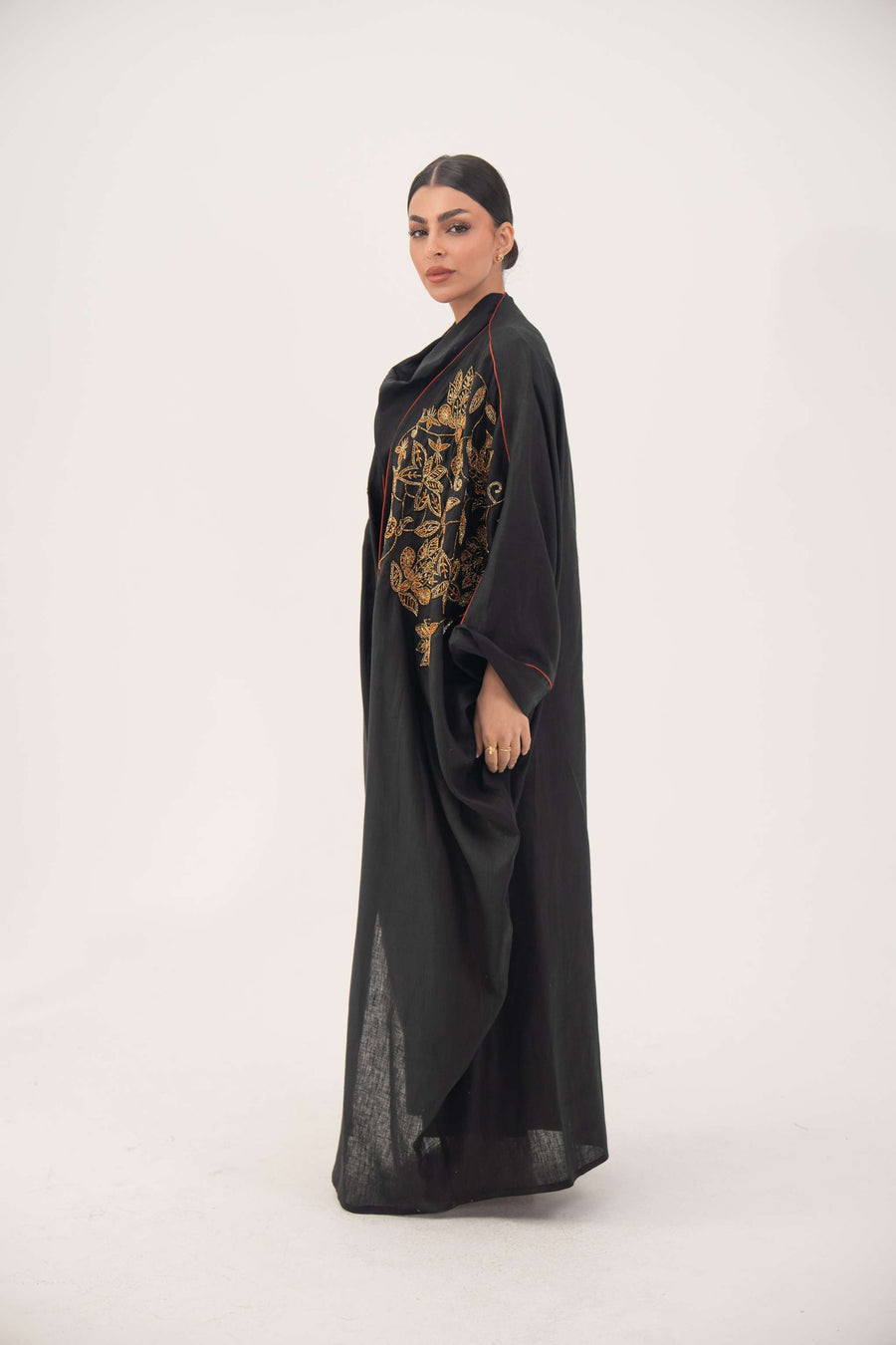 Elegant black bisht abaya with golden bronze shak embroidery and subtle orange seam detailing, made from lightweight breathable linen.