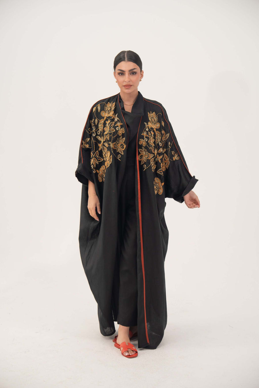 Black Bisht Abaya with gold and bronze embroidery, loose open-front design, rolled cuffs, and subtle orange trim, modeled by woman
