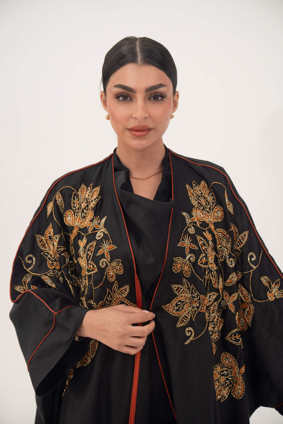 Black bisht abaya with gold and bronze floral embroidery and orange rim on wide sleeves, lightweight linen fabric, open front design.