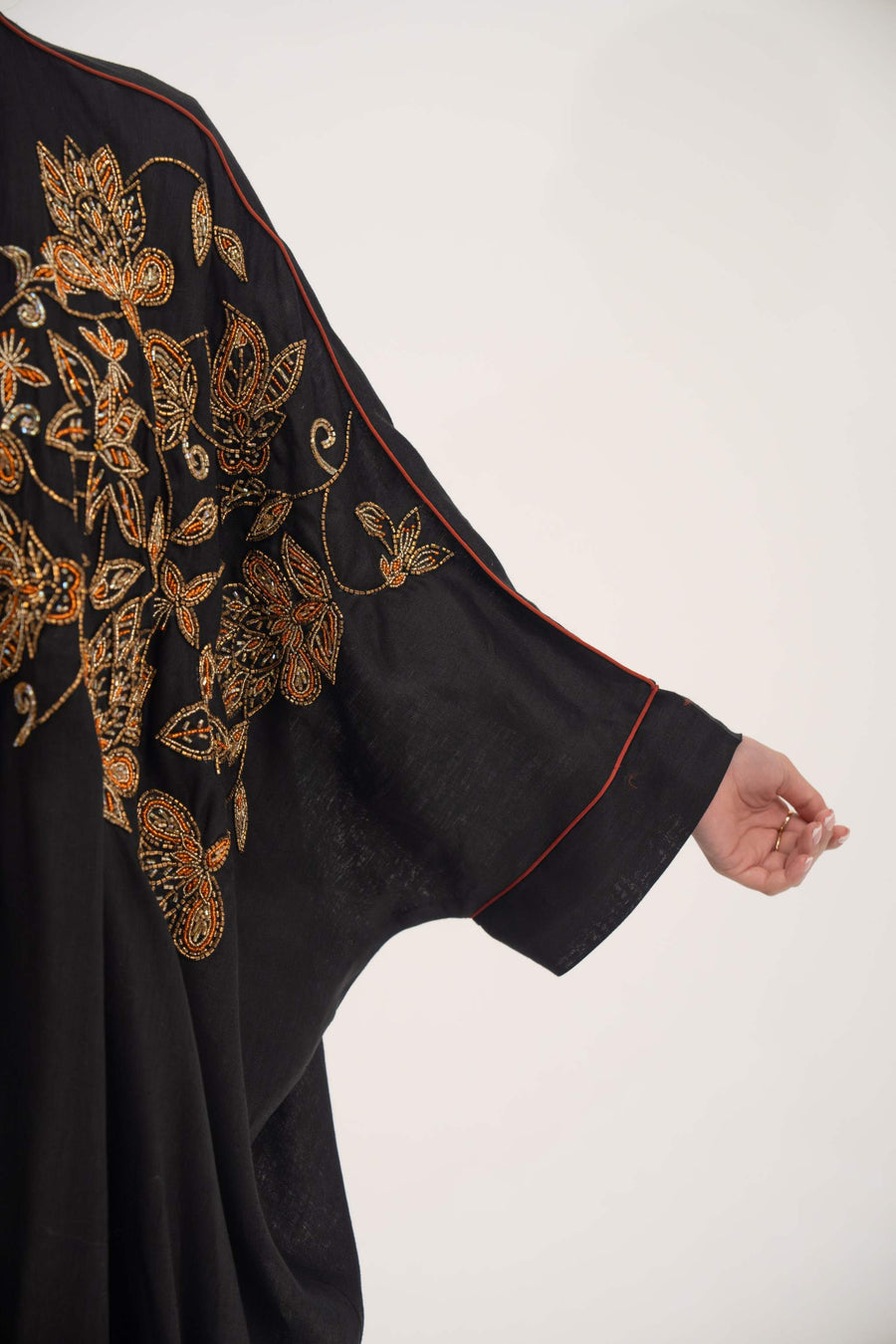 Close-up of black linen bisht abaya sleeve with golden and bronze floral embroidery and subtle orange trim