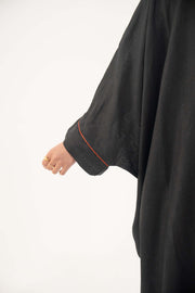 Close-up of a black linen bisht abaya sleeve with rolled cuff and subtle orange trim.