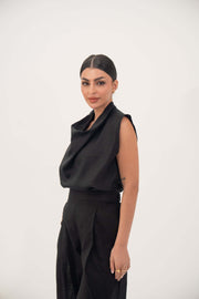Woman wearing sleeveless black linen blouse with draped neckline and subtle pleats
