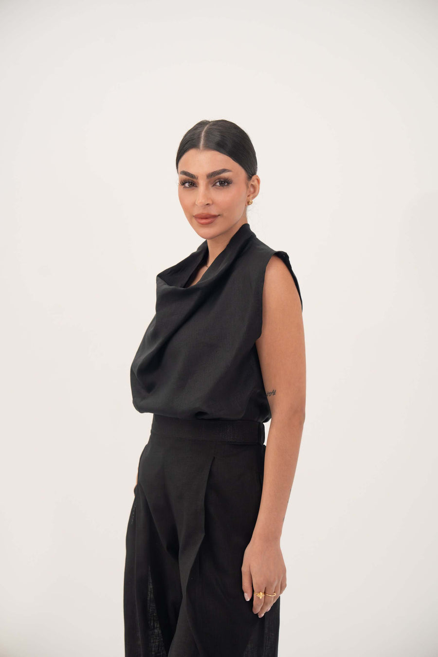 Woman wearing sleeveless black linen blouse with draped neckline and subtle pleats