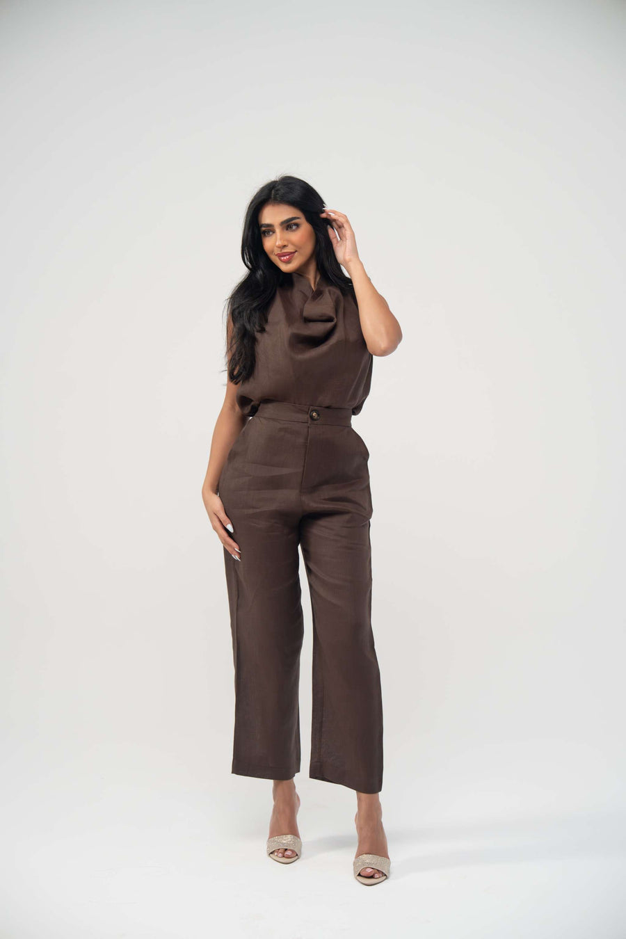 Woman wearing espresso brown sleeveless linen blouse with draped neckline and matching high-waisted pants
