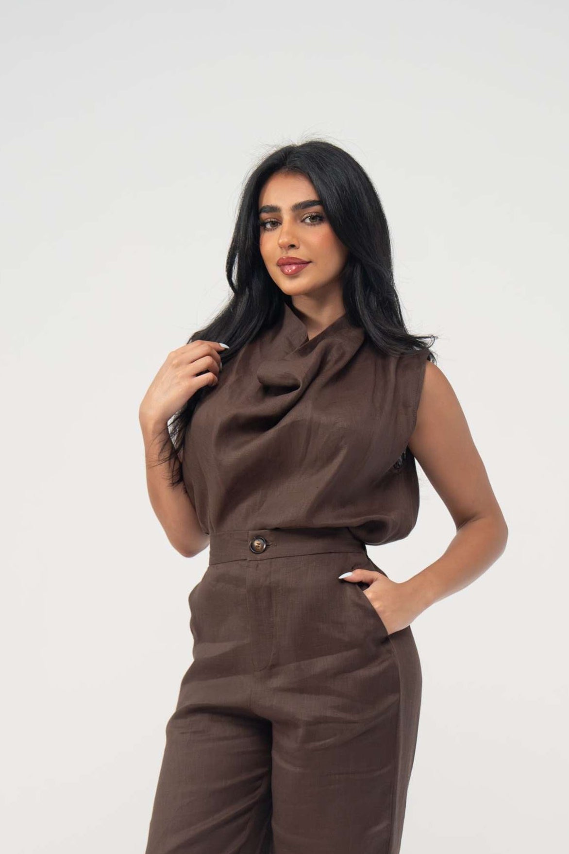 Woman wearing sleeveless warm brown espresso linen blouse with soft draped neckline and light pleats paired with matching pants
