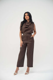 Woman wearing sleeveless warm brown espresso linen blouse with draped neckline and light pleats paired with matching pants and beige heels