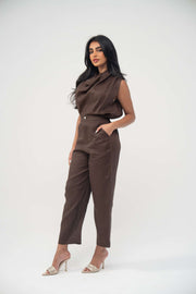 Woman wearing sleeveless warm brown linen blouse with draped neckline and pleats paired with matching pants.