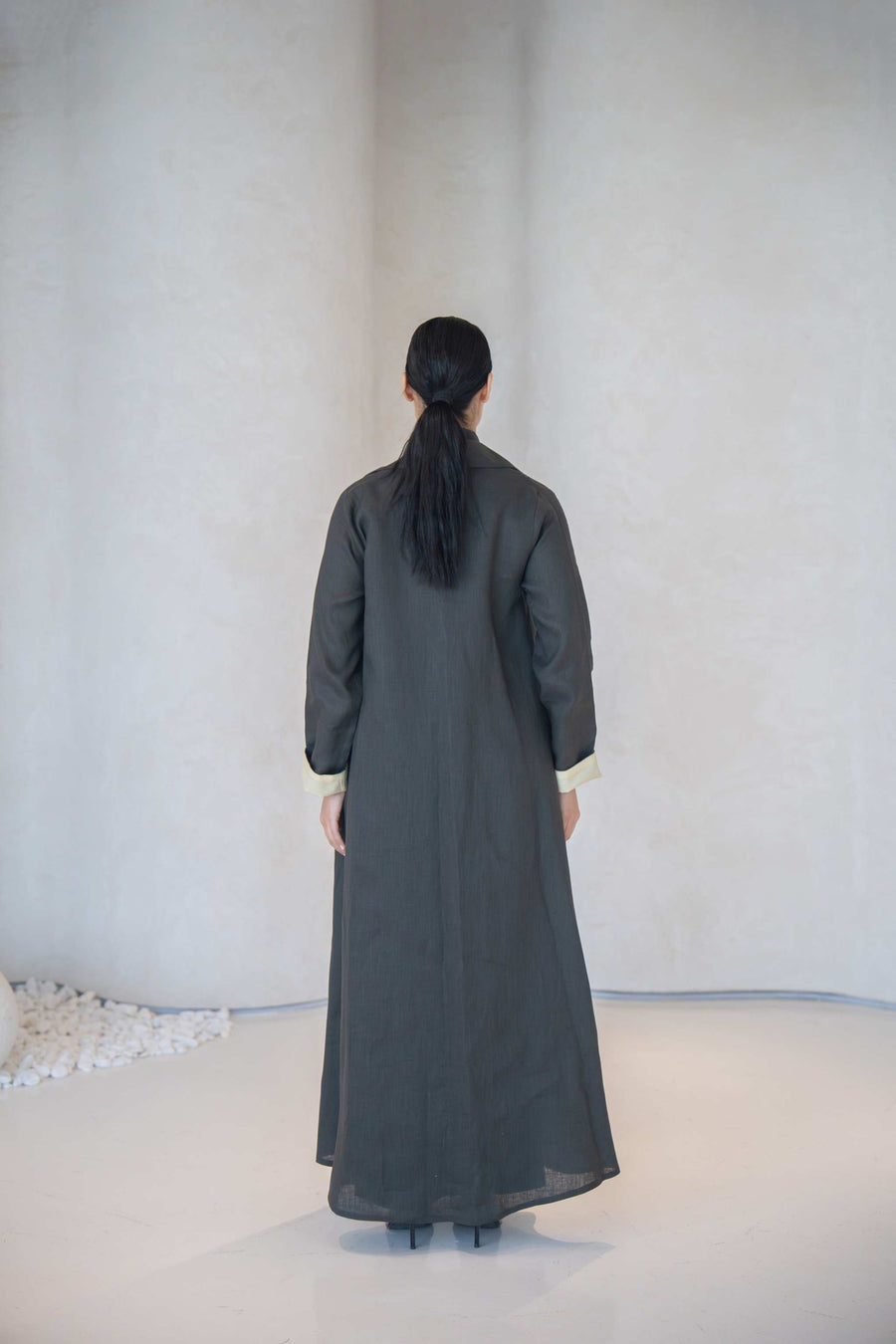 Back view of charcoal gray blazer-style abaya with soft pastel yellow cuff lining and side pocket on lightweight linen fabric
