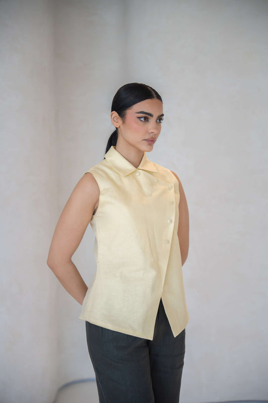 Woman wearing a sleeveless butter yellow vest with an asymmetric front and fabric-covered buttons