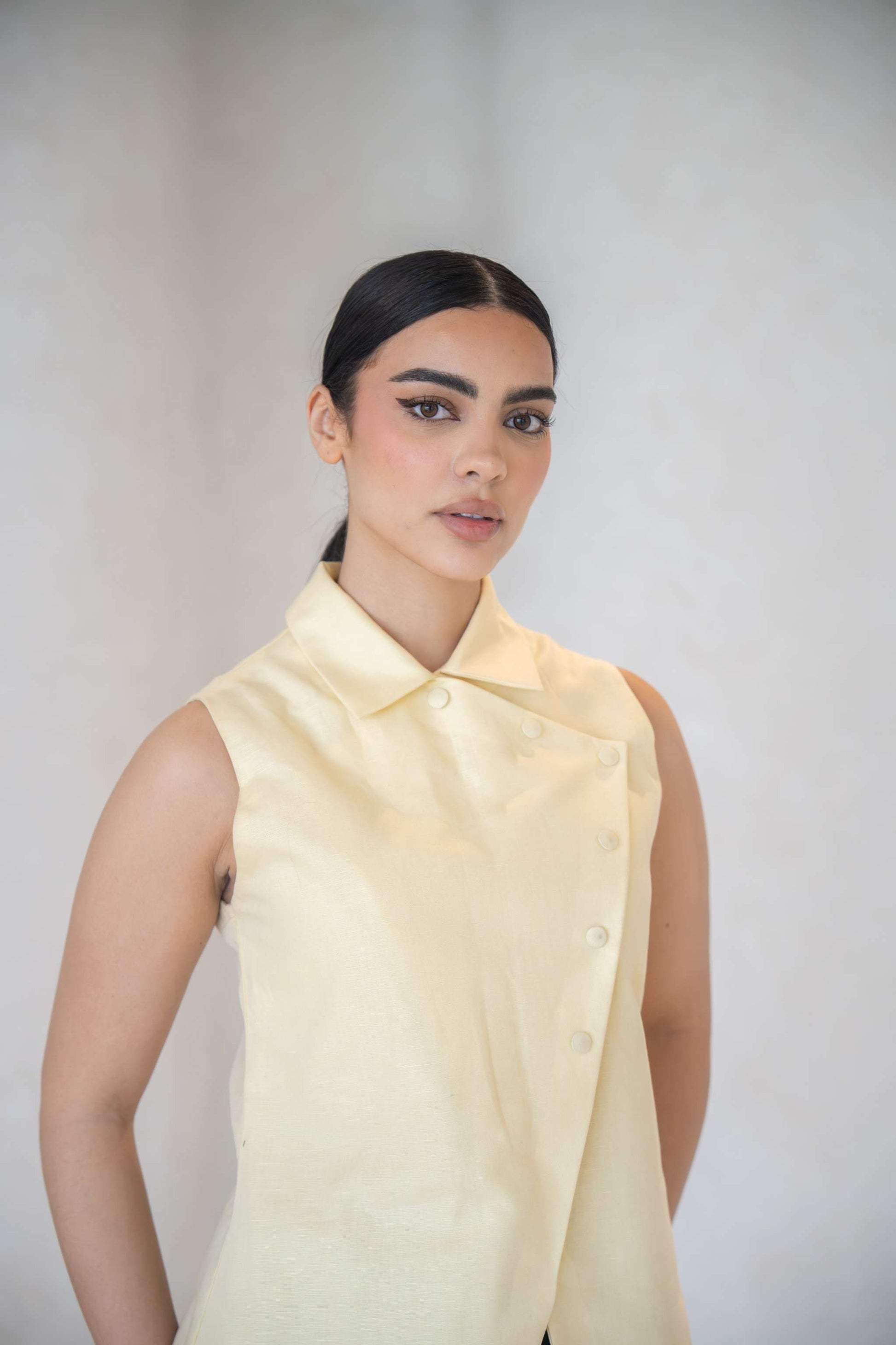 Woman wearing a sleeveless butter yellow linen vest with an asymmetric front and fabric-covered buttons-Butter Yellow Vest
