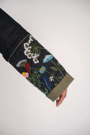 Close-up of black abaya sleeve with intricate handmade floral embroidery in multiple colors and olive green cuff trim.
