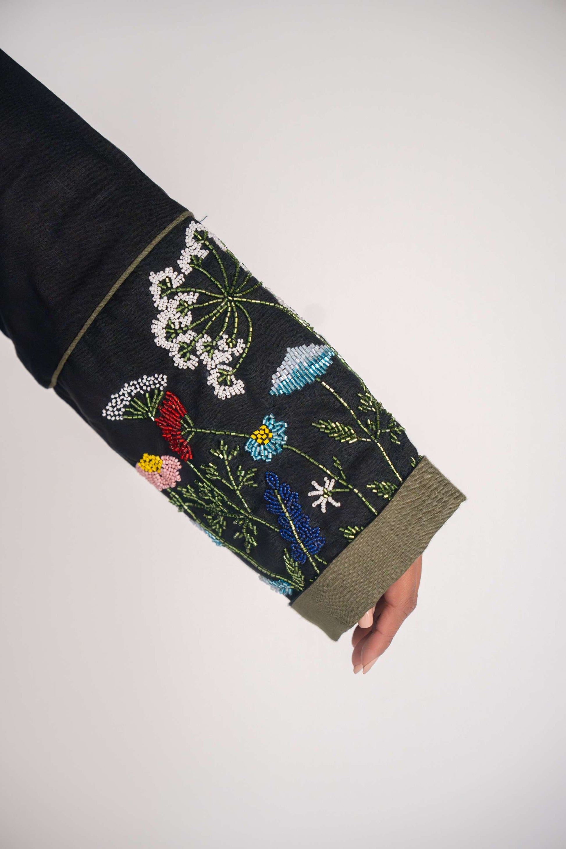 Close-up of black abaya sleeve with intricate handmade floral embroidery in multiple colors and olive green cuff trim.