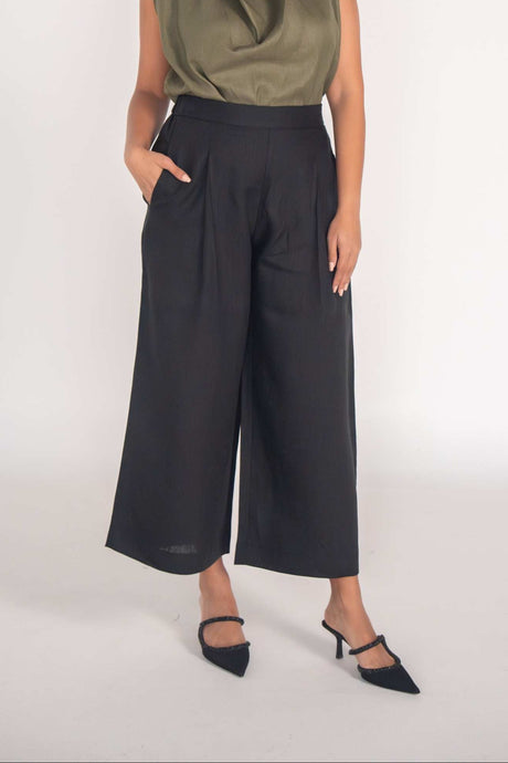 Woman wearing olive-green Raya Blouse sleeveless linen top paired with black wide-leg pants and black heels.