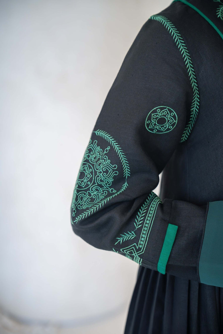 Black Zamurd abaya with green geometric embroidery on sleeves and shoulders, lightweight linen fabric with soft chiffon lining.