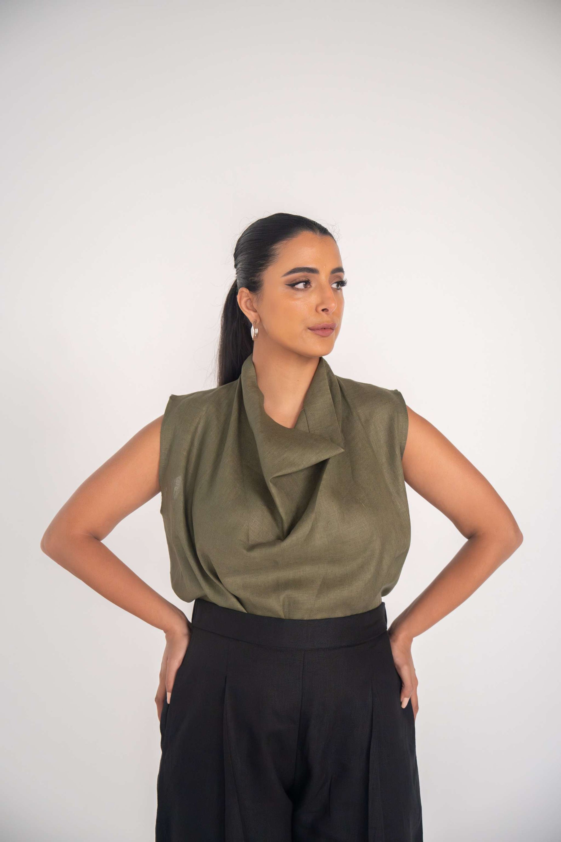 Woman wearing olive green sleeveless linen Raya blouse with relaxed fit and black high-waisted trousers