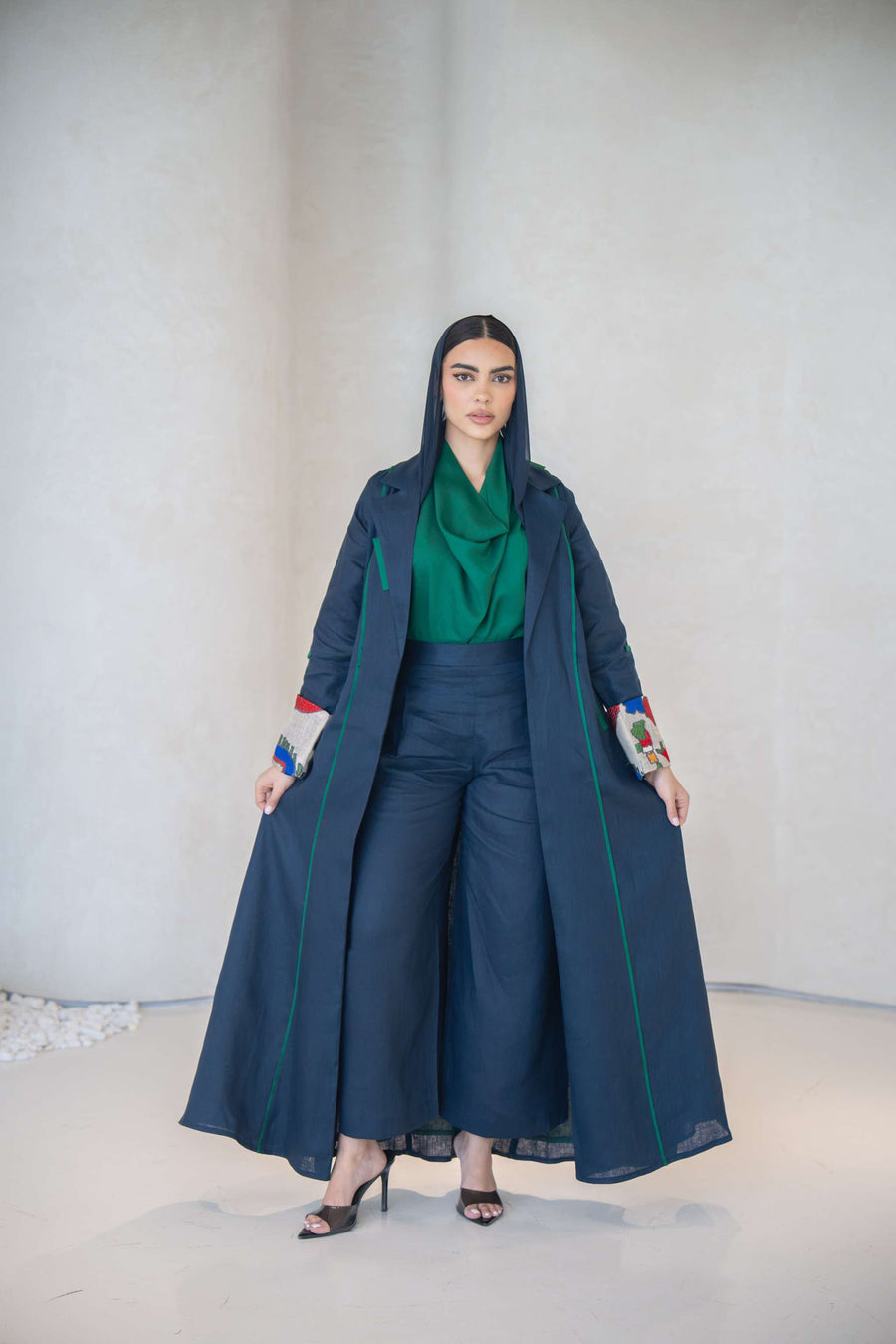 Woman wearing a deep navy abaya made of lightweight linen with emerald green accents and multicolor embroidered cuffs.