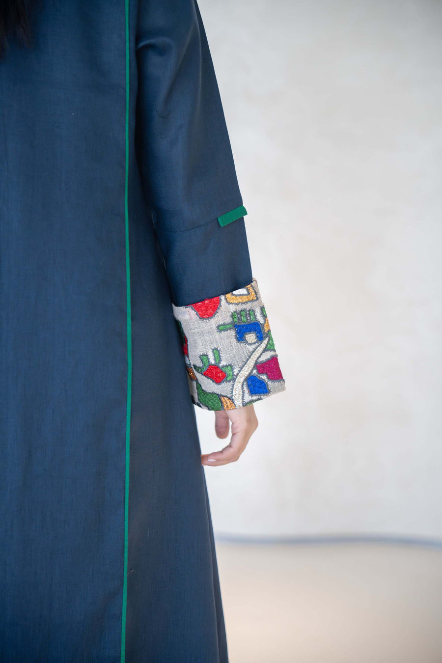 Deep navy linen abaya with emerald green piping and multicolor embroidered cuffs, featuring a modern open-front design and tailored silhouette.