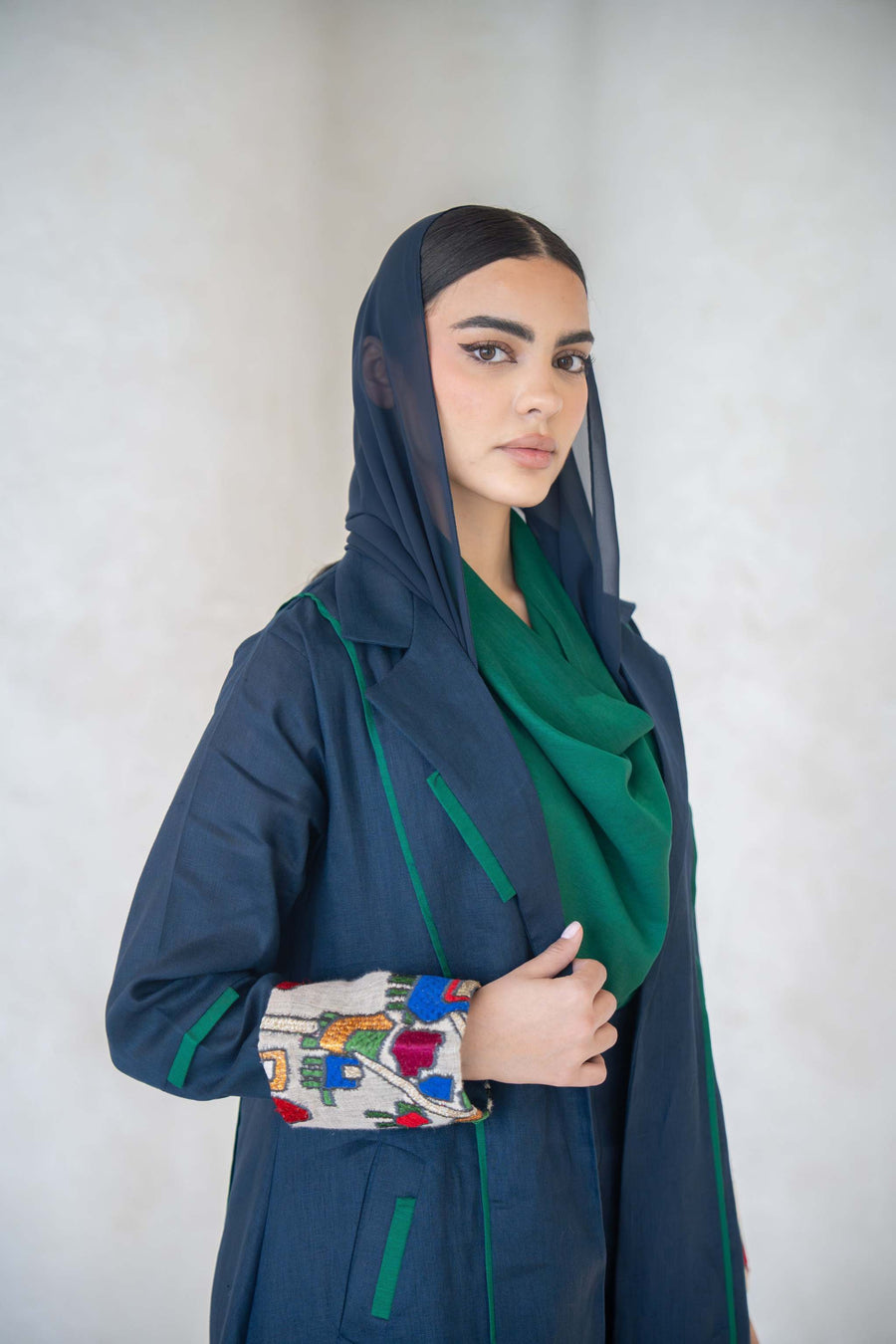 Deep navy linen abaya with emerald green piping and multicolor embroidered cuffs, featuring a modern open-front design and tailored silhouette.