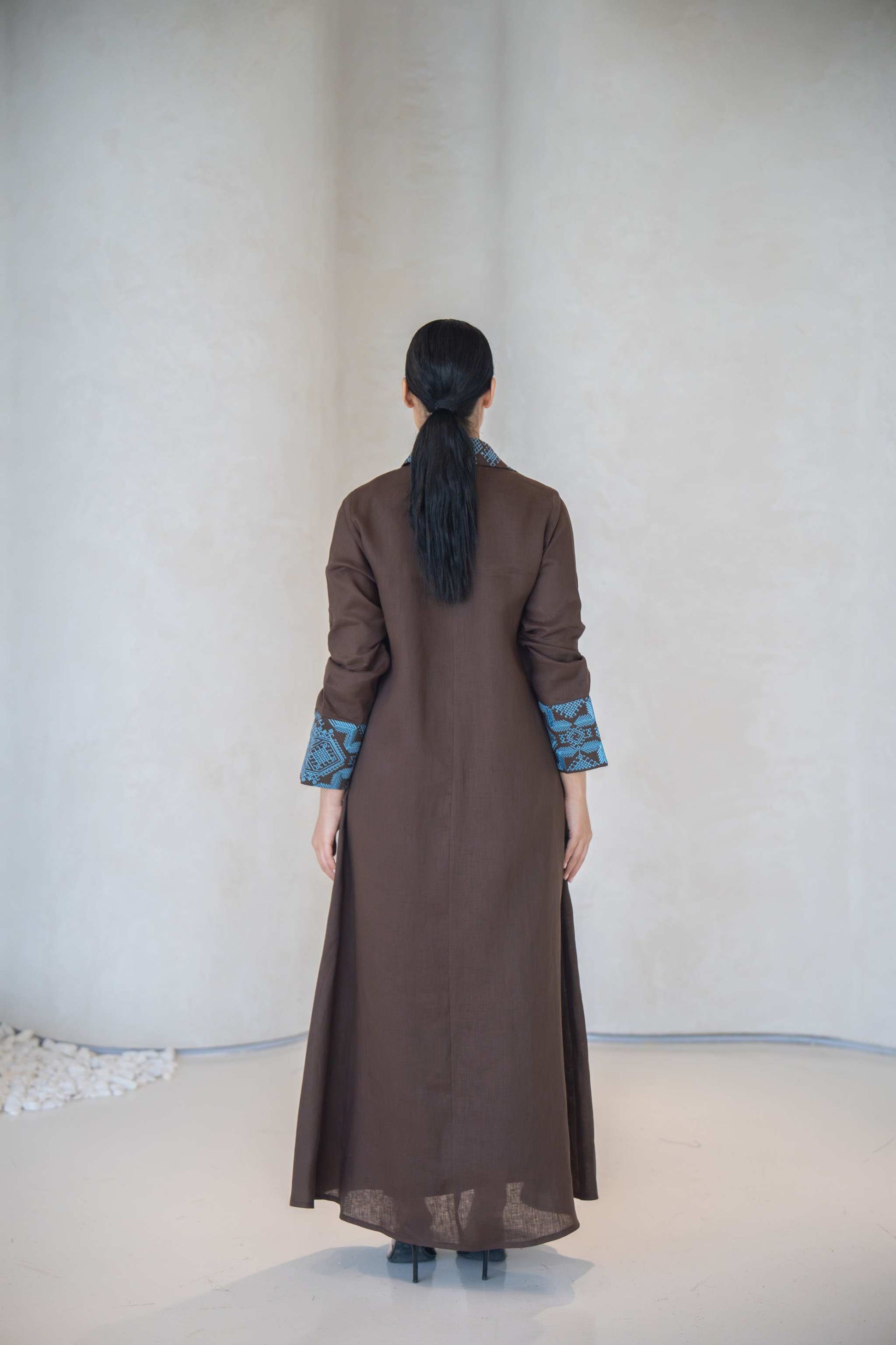Back view of a calm brown abaya with vertical turquoise embroidery on the cuffs and a structured cut, made from lightweight soft fabric for elegant comfort abaya in a calm brown