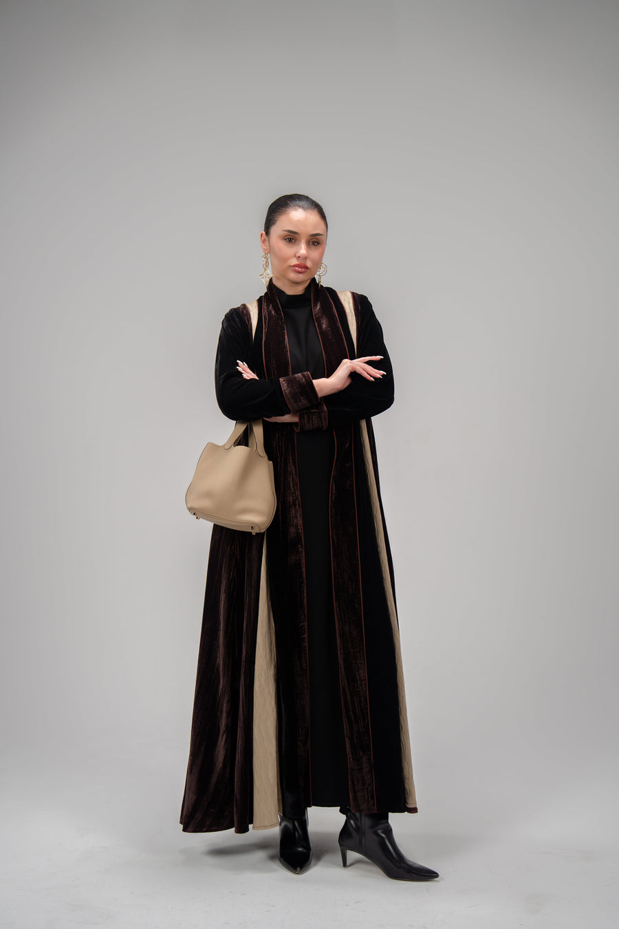 Elegant dark velvet abaya with machine embroidery and crinkled fabric details, worn by woman with beige handbag and black boots