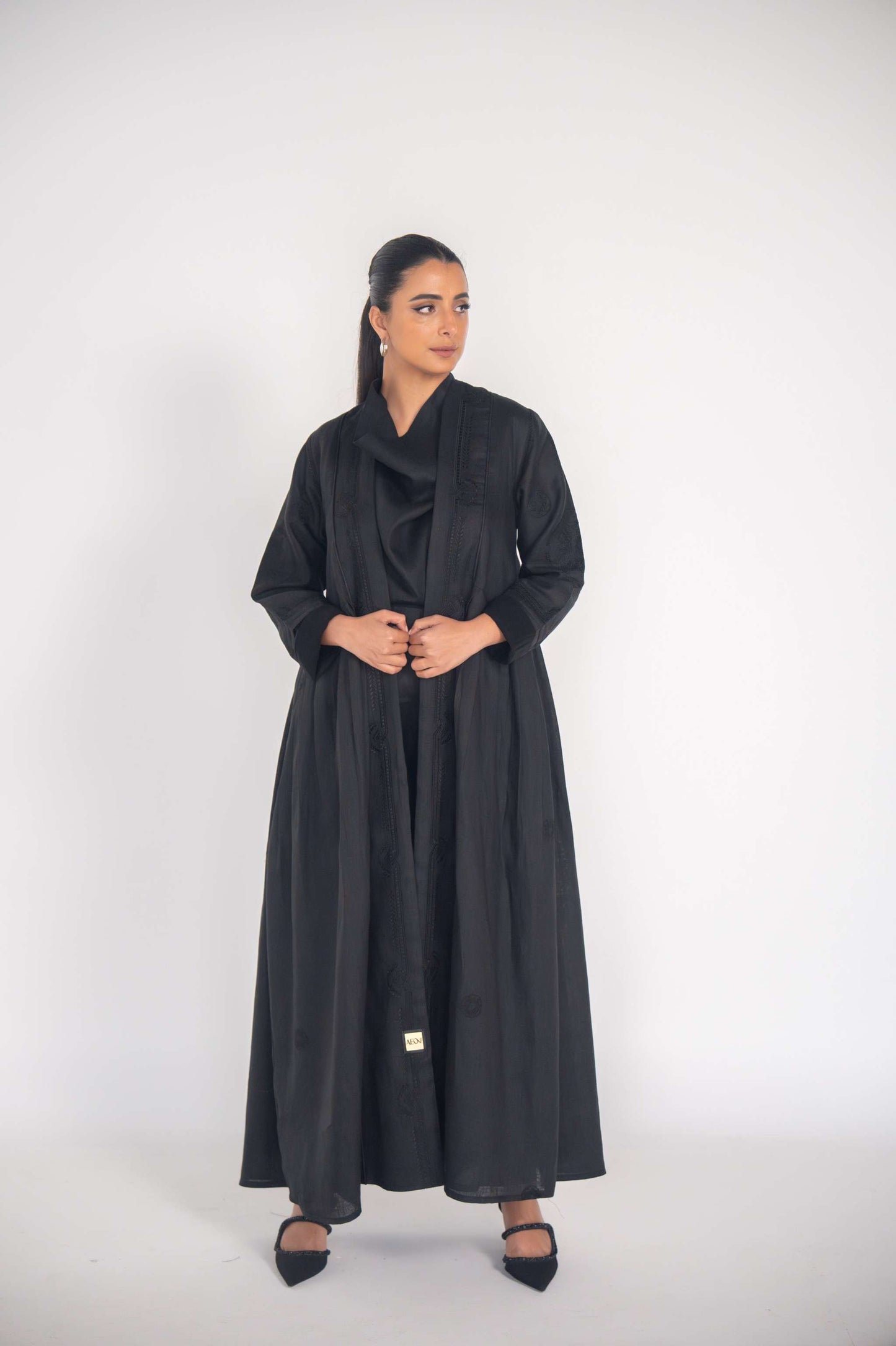 Elegant black refined abaya with breathable linen fabric, side pleats, and subtle black-on-black embroidery.