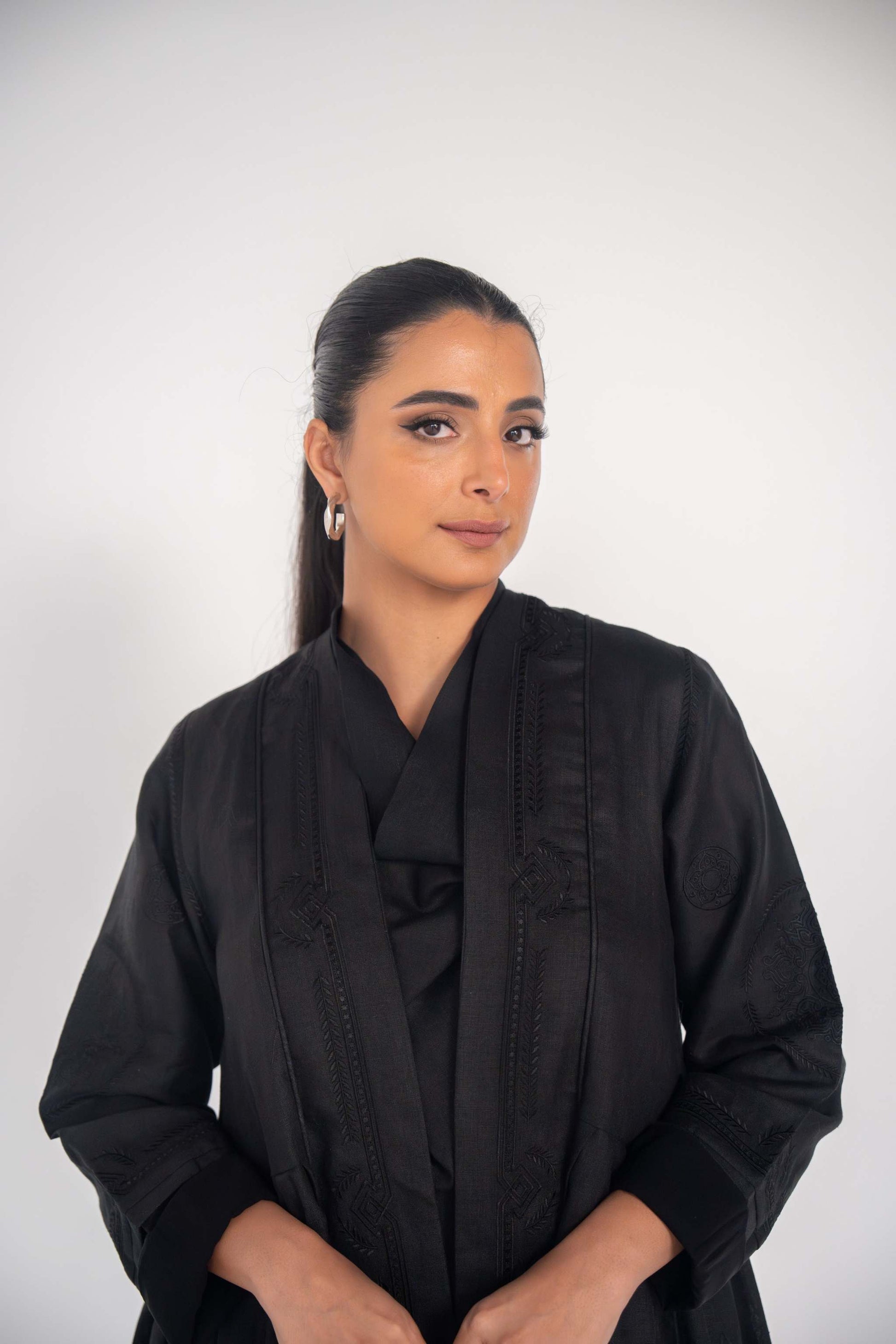 Woman wearing a black linen abaya with soft pleats and delicate black-on-black embroidery, styled for a refined and elegant look
