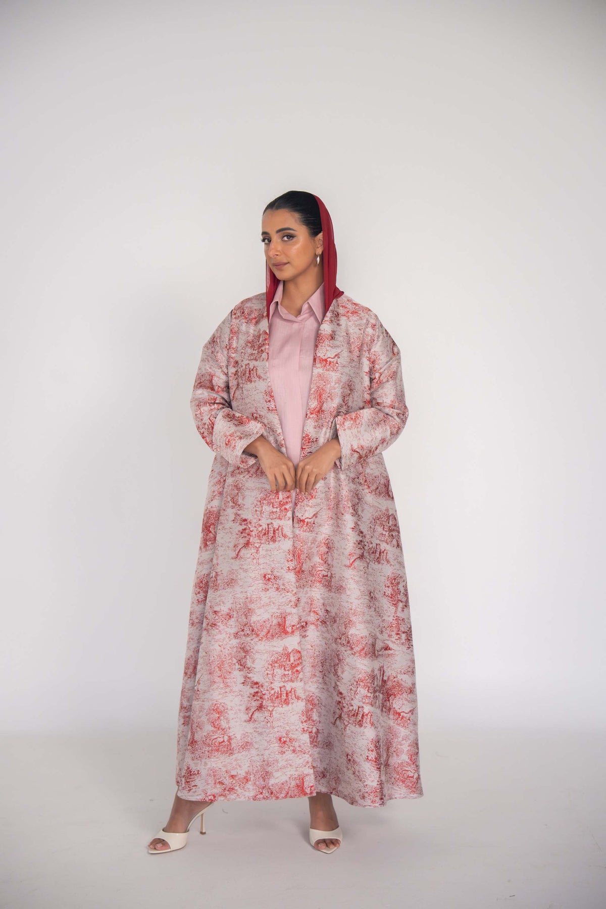Elegant Cherry Haneen jacquard abaya with red Toile de Jouy pattern on off-white fabric, featuring detailed countryside illustrations and flowing tailored sleeves.