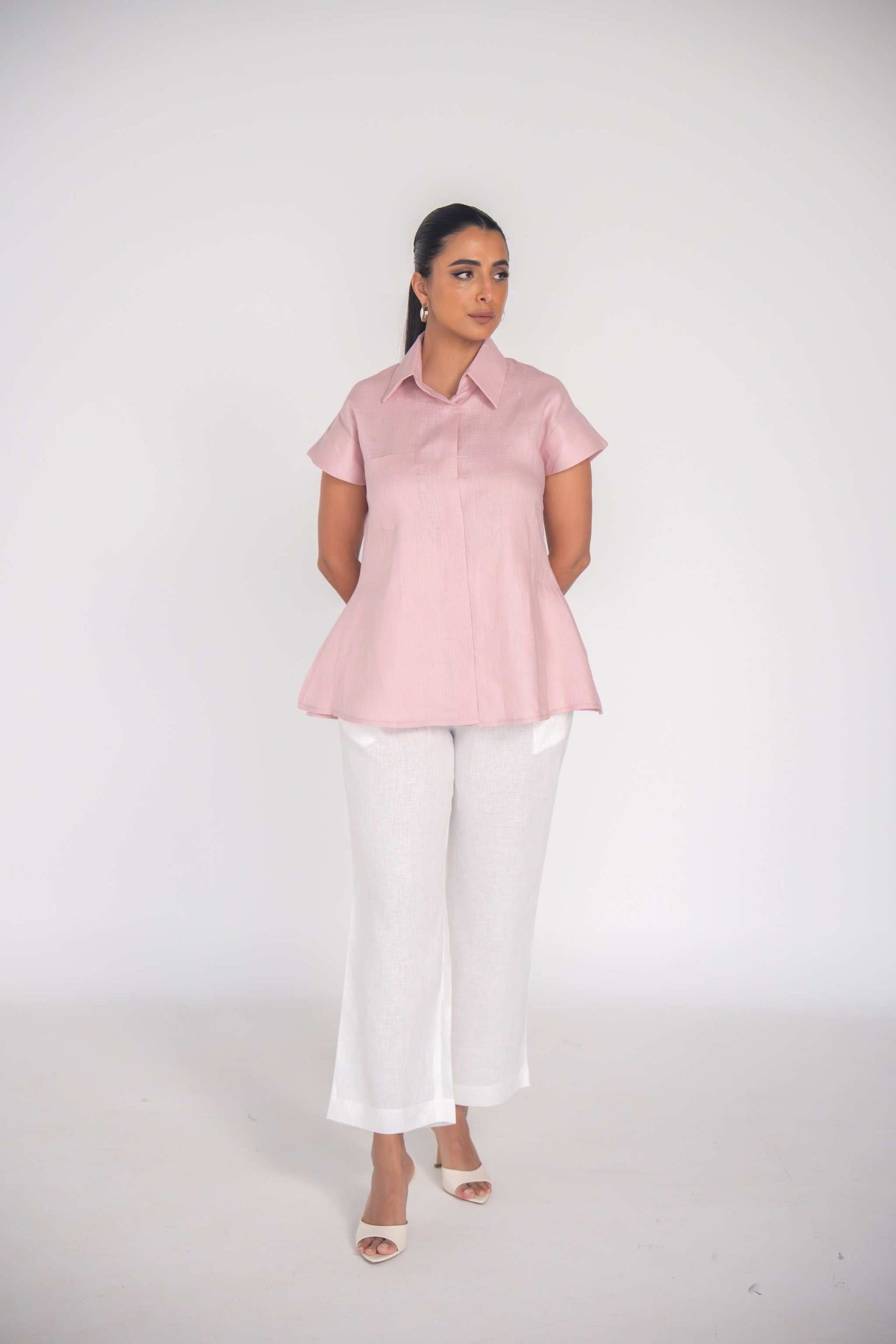 woman wearing soft pink linen collar shirt with short sleeves and white pants standing on white background