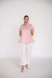 Woman wearing a soft pink collar shirt paired with white trousers against a light background