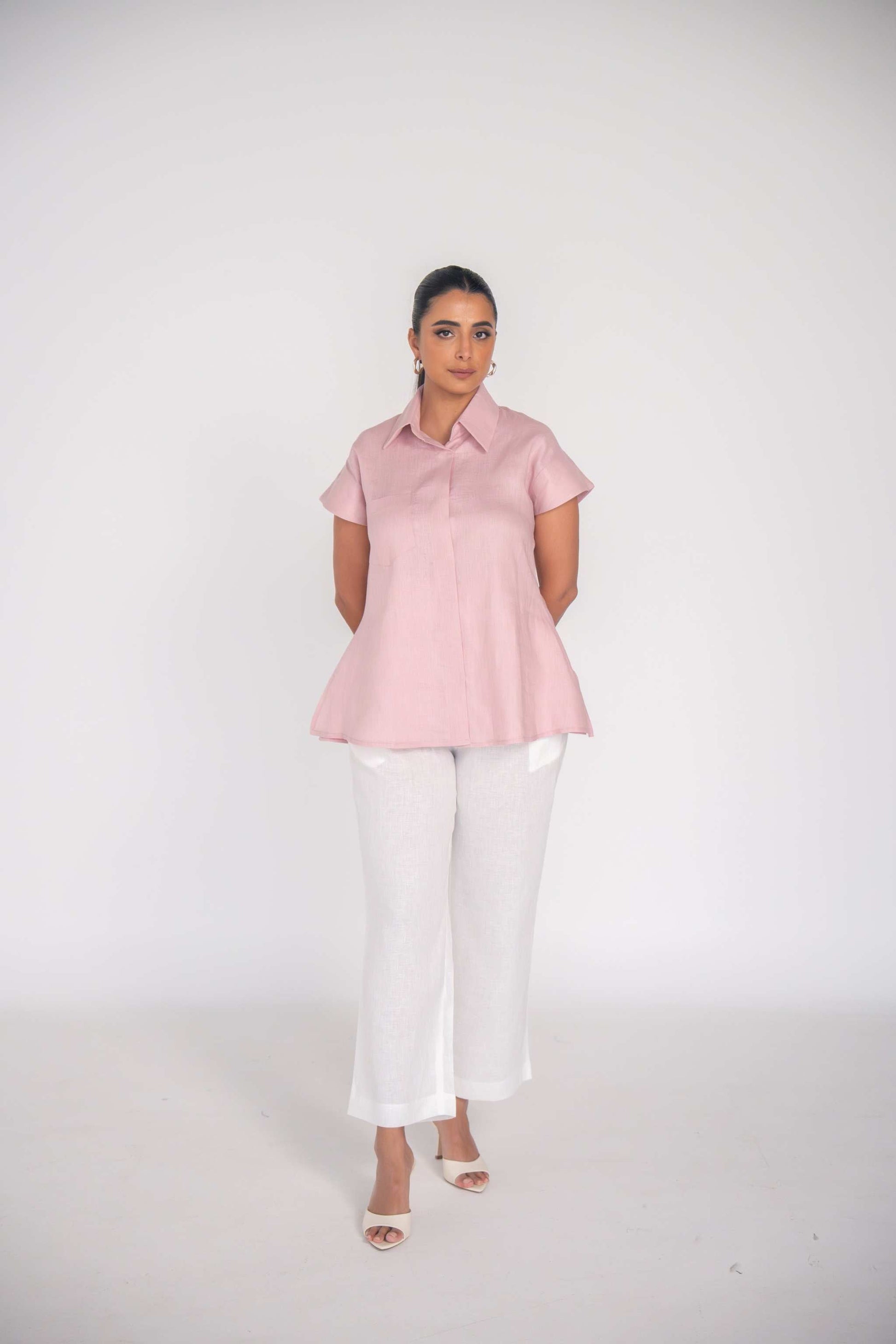 Woman wearing a soft pink collar shirt paired with white trousers against a light background