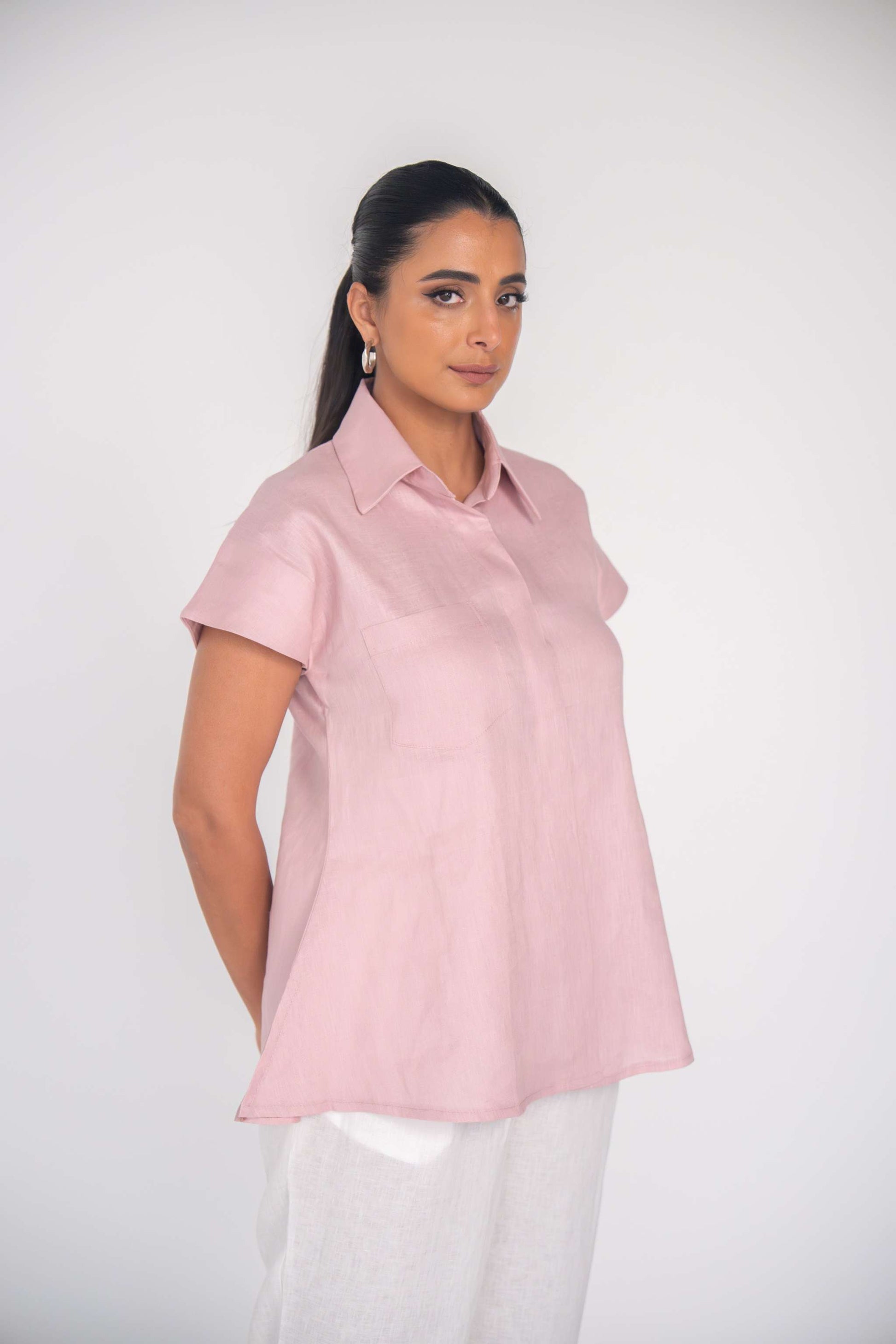 Woman wearing a soft pink linen collar shirt with short sleeves and flared silhouette.