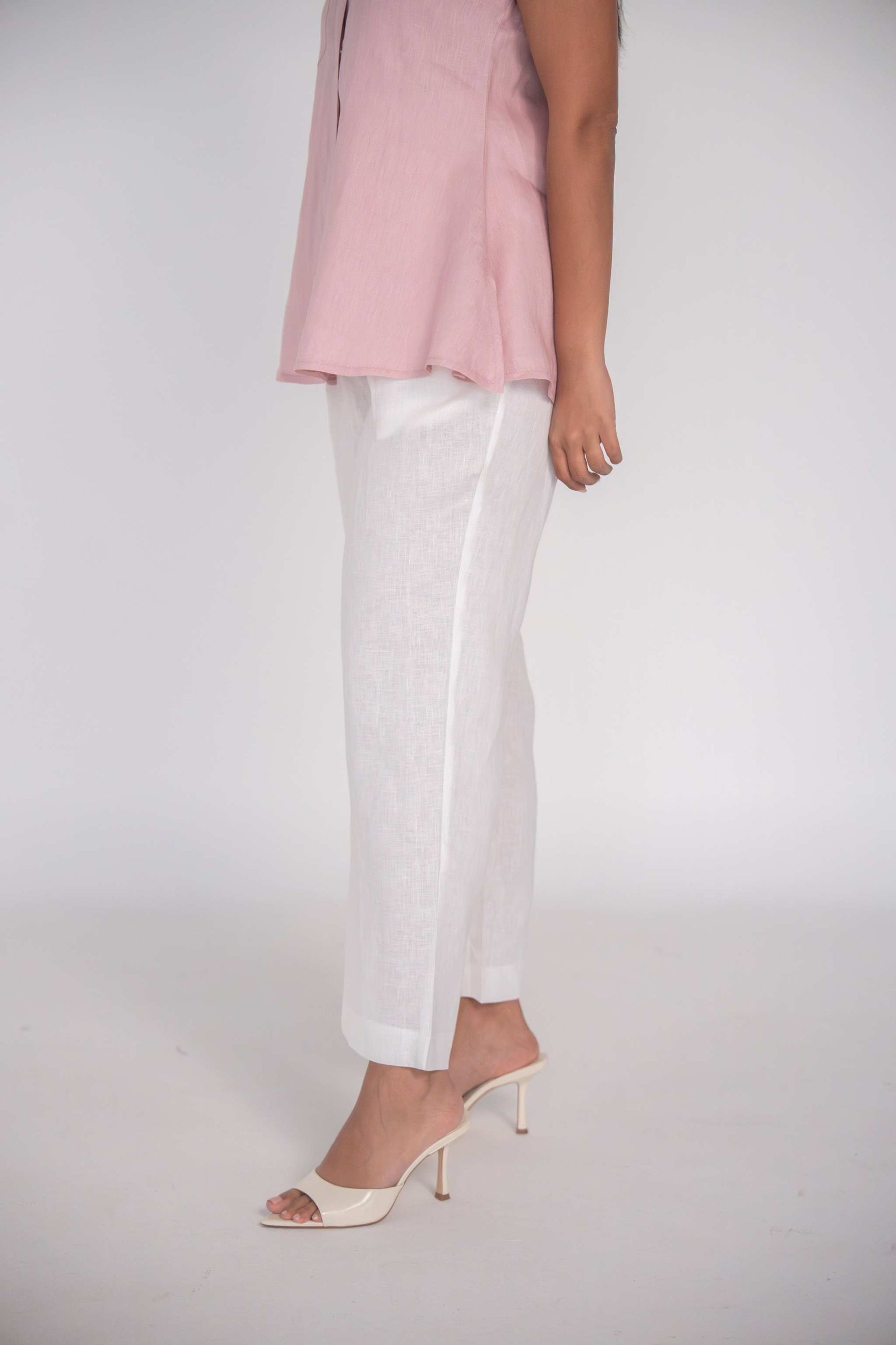 Woman wearing white linen pant with straight cut and cuffed hem paired with pink top and beige heeled sandals