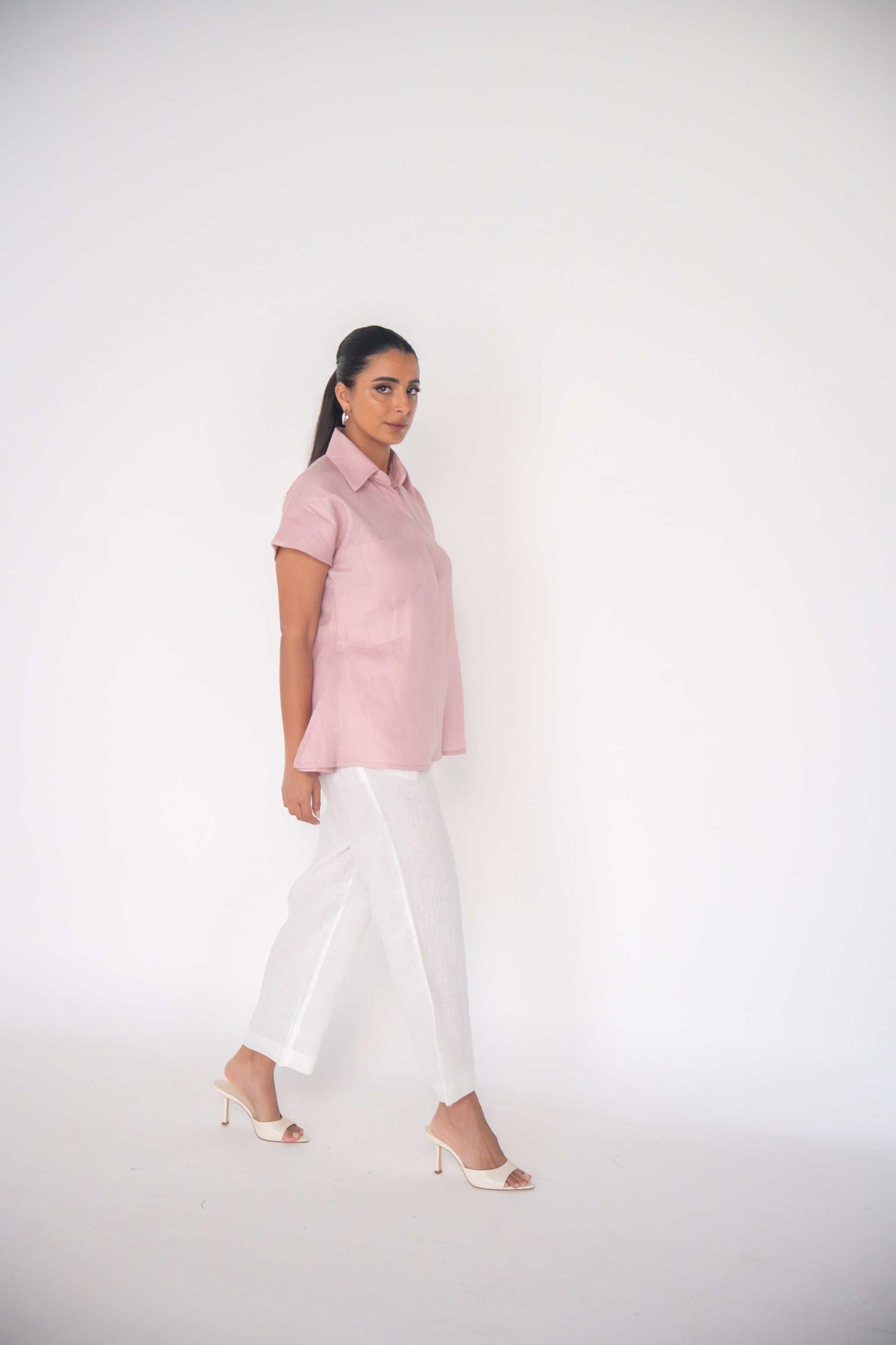 Woman wearing white linen pants with a straight cut and a pink short-sleeve shirt, styled for warm weather.